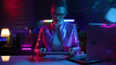 Neon metaevren fütüristik konsepti. Modern ofiste bilgisayarlı ve tabletli gözlüklü modern iş kadını..