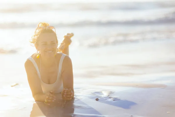 身穿白色泳衣的快乐优雅的女人躺在海滩上 — 图库照片