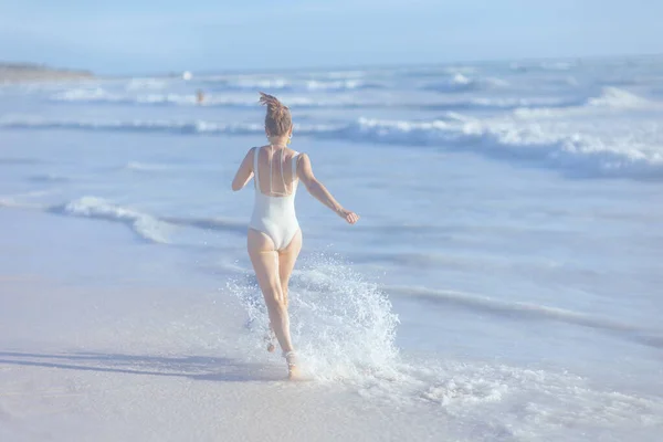 从40岁身穿白色泳衣的现代女子身后看到海滩上欢乐的景象 — 图库照片