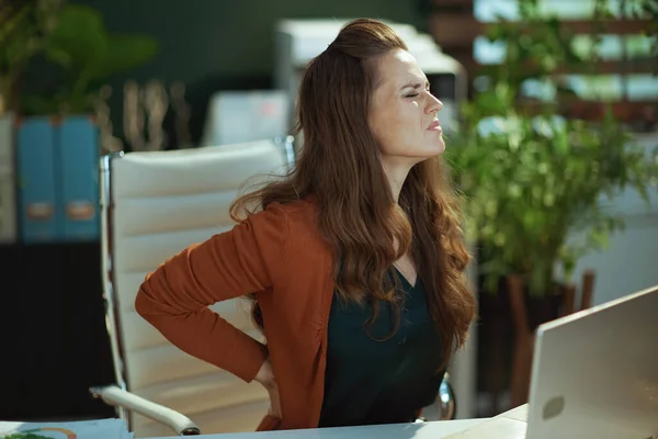 現代の緑のオフィスで腰痛を持つ悲しい現代中小企業経営者女性 — ストック写真