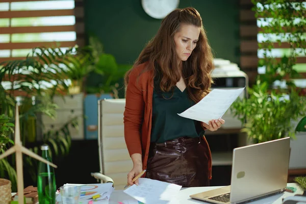 現代のグリーンオフィスで書類を扱うノートパソコンを持つ若い中小企業経営者の女性 — ストック写真
