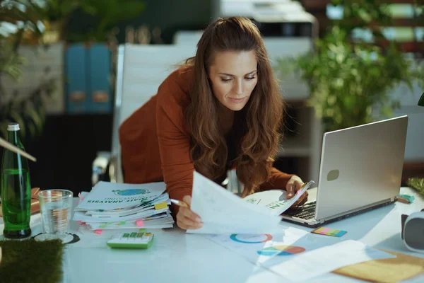 若いです40歳の小さなビジネスの所有者の女性ノートパソコンと現代の緑のオフィスで文書を扱う女性 — ストック写真