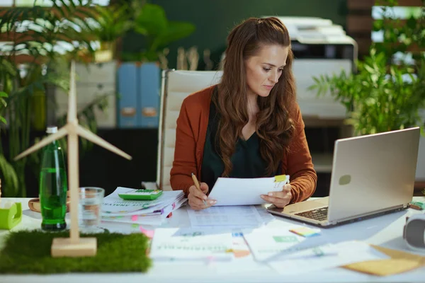 現代のグリーンオフィスで書類を扱うノートパソコンを持つトレンディーな中小企業の所有者の女性 — ストック写真