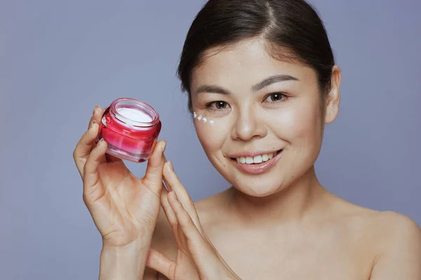 顔のクリーム瓶と顔のクリームを持つ現代アジアの女性の肖像画青の背景に顔 — ストック写真
