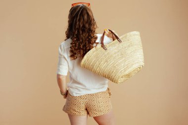 Plaj tatili Beyaz bluzlu, şortlu, bej arka planda saman çantalı ve güneş gözlüklü bir kadın görüldü..