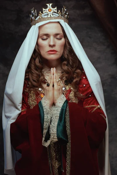 穿着红色衣服 头戴面纱 头戴皇冠的中世纪女王在深灰色背景下祈祷 — 图库照片