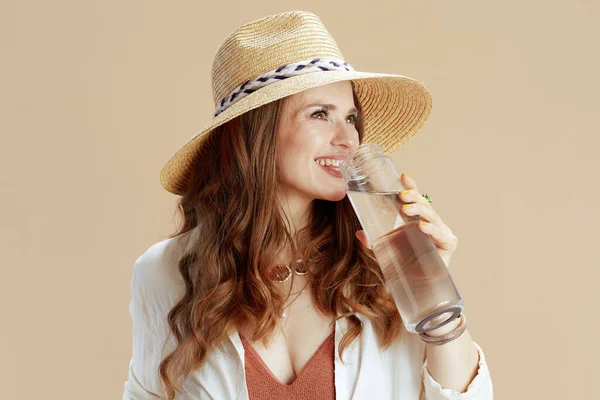 ビーチ休暇 幸せな現代的な中年主婦で白いブラウスとショートパンツ隔離上のベージュでボトルの水と夏の帽子 — ストック写真