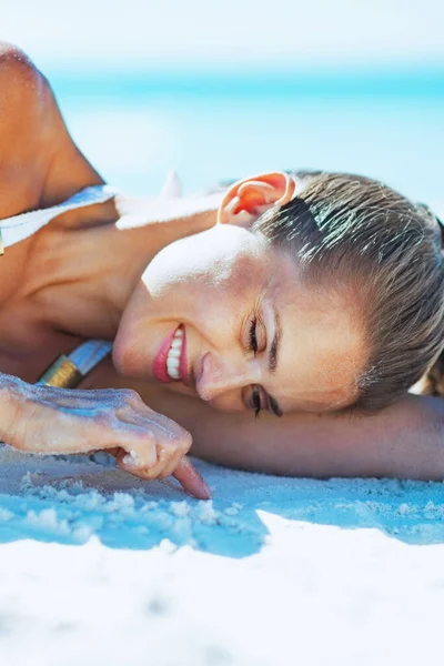 幸福的年轻女人在泳装躺在沙滩上和玩沙子 — 图库照片
