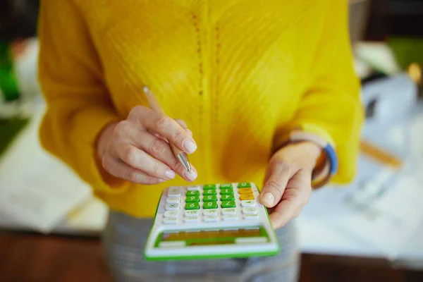 穿着黄色毛衣 绿色办公室里拿着计算器的小企业主女人的衣服 — 图库照片