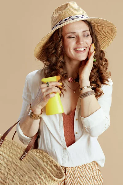 ビーチ休暇 現代的な笑顔40歳の主婦で白いブラウスとショートパンツでベージュを背景にストローバッグ 日焼け止めと麦わら帽子 — ストック写真