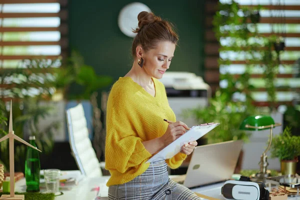 現代の緑のオフィスでクリップボードと黄色のセーターの流行の中小企業の所有者の女性 — ストック写真
