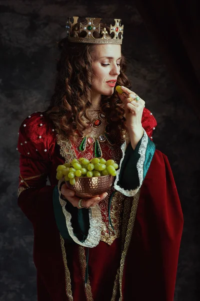 中古时代的女王 身穿红色衣服 有一盘葡萄 头戴深灰色背景的皇冠 — 图库照片