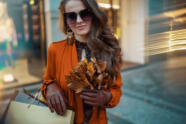 10月份 全市商店附近穿着褐色风衣 头戴购物袋 头戴秋天黄色叶子的年轻女子 — 图库照片