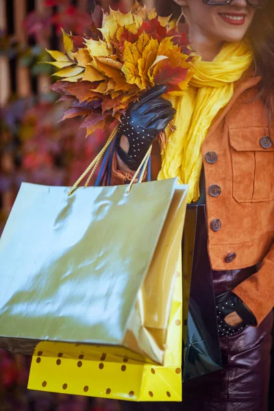10月だ 40歳の女性を笑顔でオレンジトレンチコートに買い物袋と秋の黄色の葉を街で — ストック写真