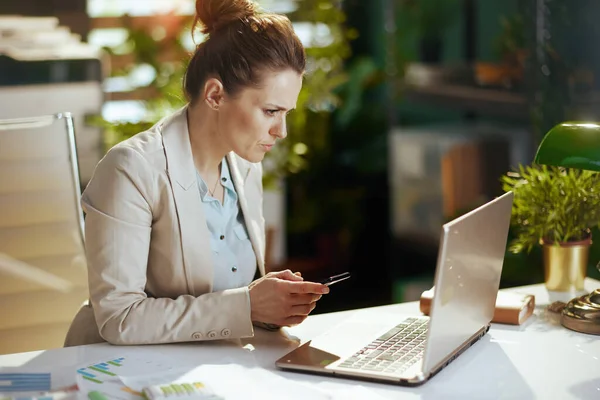 modern accountant woman in a light business suit in modern green office with laptop and smartphone.