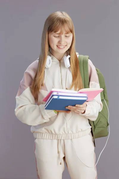 ベージュ トラックスーツに身を包んだ現代の女の子を笑顔でバックパックやワークブック ヘッドフォンで — ストック写真