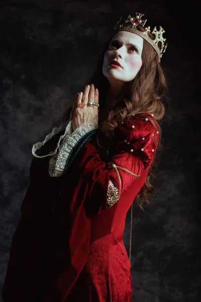 穿着红色衣服 头戴皇冠的中世纪女王在深灰色背景下祈祷 — 图库照片