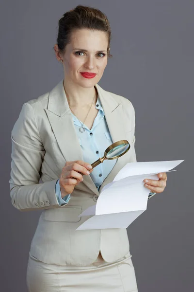 ビジネススーツを着たスタイリッシュな女性虫眼鏡と灰色の背景に隔離された文書 — ストック写真