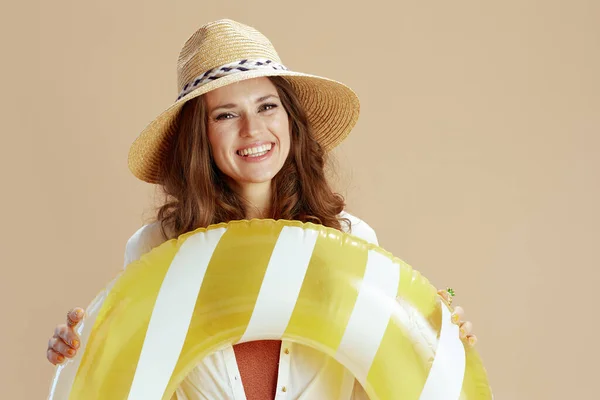 海滩度假 穿着白衬衫和短裤的优雅的中年家庭主妇 穿着米黄色背景的衣服 戴着充气圆圈和夏帽 面带微笑 — 图库照片
