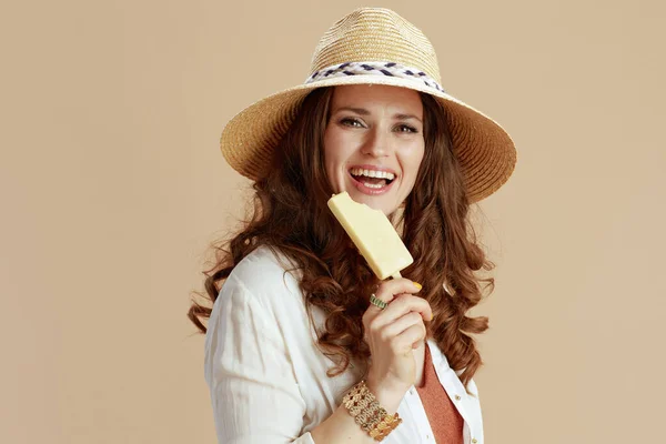 ビーチ休暇 白のブラウスにベージュの背景にアイスクリームと麦わらの帽子で隔離されたショーツで流行の女性を笑顔 — ストック写真