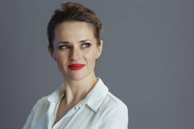 Beyaz bluzlu, modaya uygun bir bayan çalışanın gri arka planda tek başına bir tarafa bakması..
