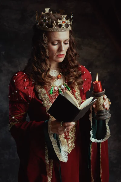中古时代的女王 穿着红色衣服 头戴深灰色背景的书 蜡烛和王冠 — 图库照片