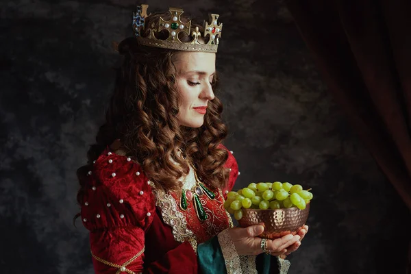 中古时代的女王 身穿红色衣服 有一盘葡萄 头戴深灰色背景的皇冠 — 图库照片