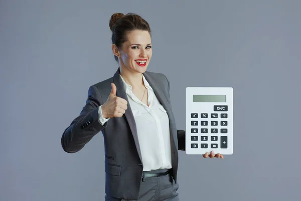 穿着灰色西装的快乐时髦的40岁女性员工 带着计算器 用灰色显示大拇指 — 图库照片