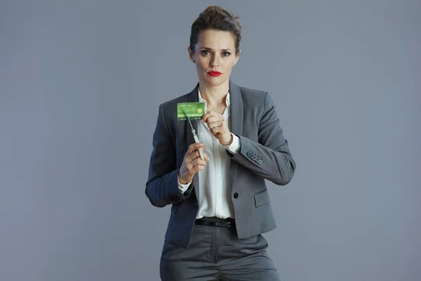 stressed young small business owner woman in gray suit with credit card and scissors isolated on gray background.