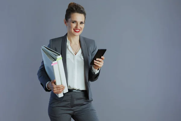 40岁的快乐优雅的小企业主女人 穿着灰色西装 有智能手机和灰色背景的文件夹 — 图库照片