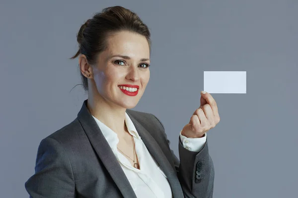 スタイリッシュな中年中小企業経営者の女性を笑顔灰色の背景に隔離された名刺付きグレースーツ — ストック写真