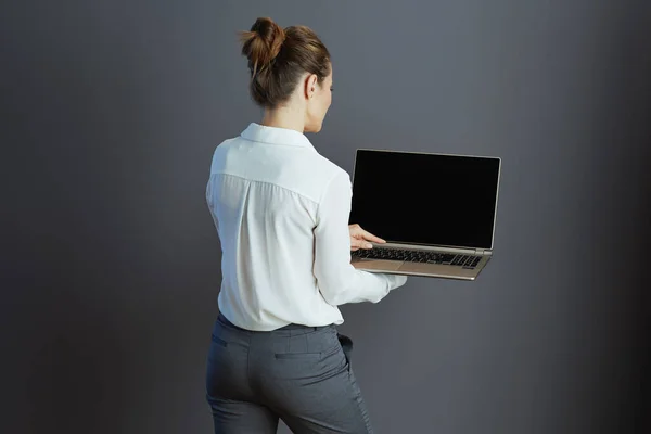 中世の後ろから見た小さなビジネス所有者女性で白いブラウスでノートパソコンでグレーの背景 — ストック写真