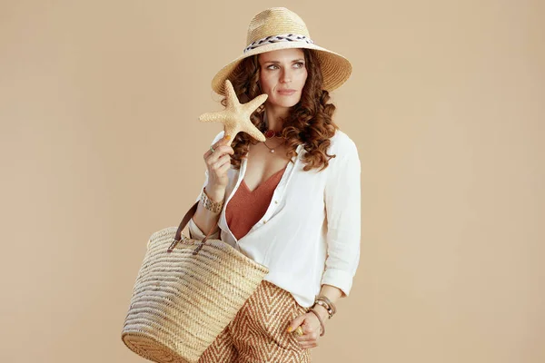 海滩度假 穿着白衬衫和短裤的时髦女人 衬托着米色背景的海星 草袋和草帽 — 图库照片
