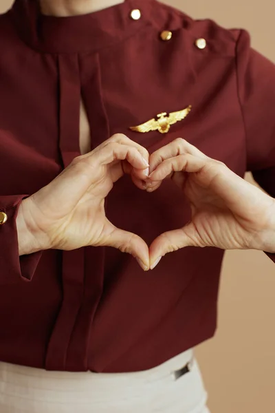 Closeup on stylish female air hostess showing heart shaped hands against beige background.