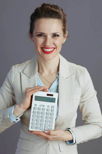 穿着浅色西装 头戴灰色背景计算器的现代中年女工面带微笑 — 图库照片