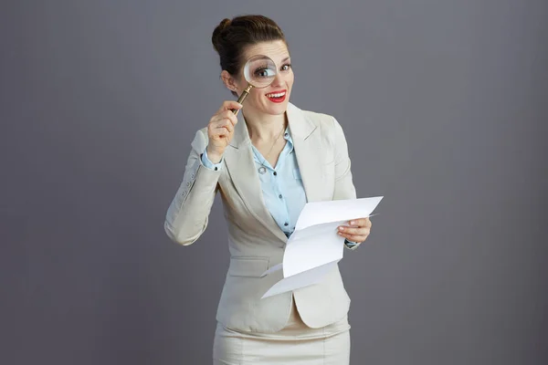 幸せな流行の小さなビジネスの所有者女性ですライトビジネススーツで虫眼鏡とグレーに隔離された文書 — ストック写真