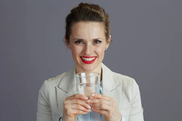 Uśmiechnięta Letnia Pracownica Lekkim Garniturze Biznesowym Szklanką Wody Szarym Tle — Zdjęcie stockowe