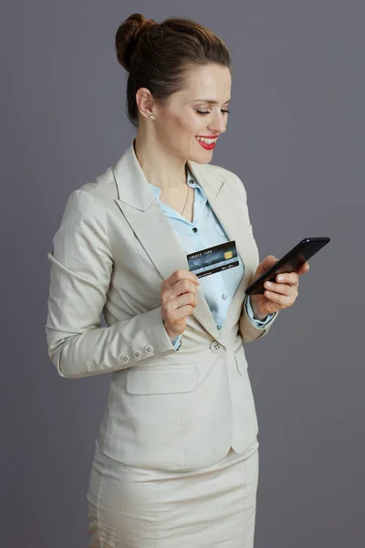 Uśmiechnięta Nowoczesna Pracownica Lekkim Garniturze Biznesowym Smartfonem Kartą Kredytową Szarym — Zdjęcie stockowe