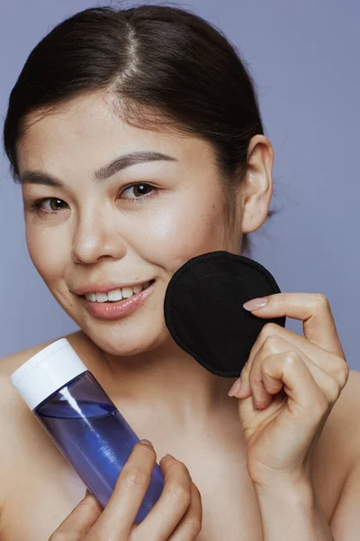 青い背景にメイク落としと黒の綿のパッドを持つ若いアジアの女性 — ストック写真