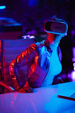 Neon metaevren fütüristik konsepti. Modern ofiste sanal gerçeklik gözlüğü takan meraklı, şık bir kadın..
