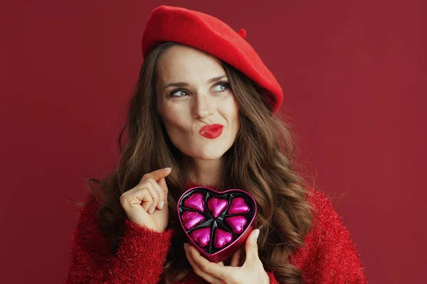 ハッピーバレンタイン 赤いセーターとベレー帽とハート型のキャンディボックスに長い波状の髪を持つ可愛い女性 — ストック写真