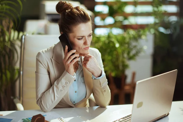 現代のグリーンオフィスのライトビジネススーツの中小企業経営者女性ノートパソコンでスマホで話してる — ストック写真