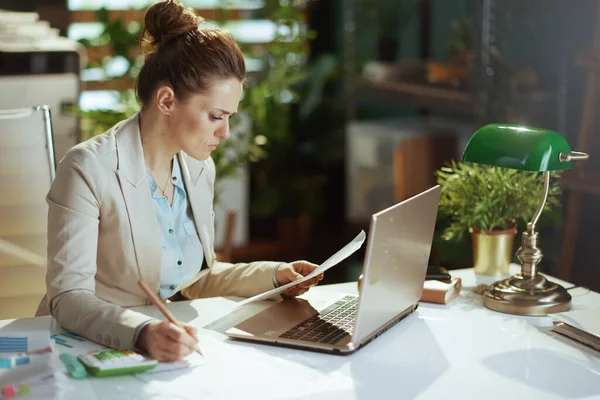 穿着轻便西服的现代女工穿着现代绿色办公室的文件和手提电脑 — 图库照片