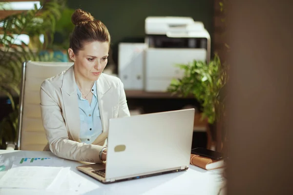 穿着轻便西装的中年妇女穿着现代绿色办公室的手提电脑 — 图库照片