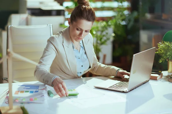 書類とノートパソコンを備えたモダンなグリーンオフィスのライトビジネススーツを着た40歳のビジネス女性 — ストック写真