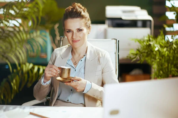 幸せな現代的な中年中小企業の所有者の肖像コーヒーカップと現代の緑のオフィスで軽いビジネススーツの女性 — ストック写真