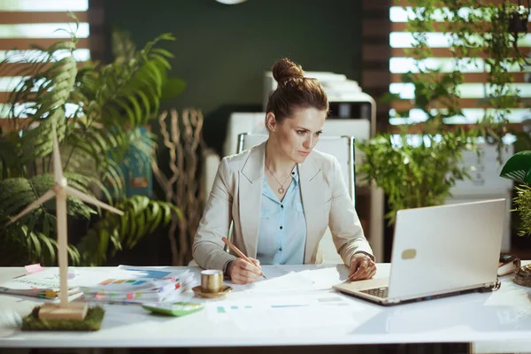 書類やノートパソコン付きのモダンなグリーンオフィスのライトビジネススーツの現代のビジネス女性 — ストック写真