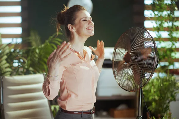 持続可能な職場 現代の40歳の女性労働者を笑顔電気ファンで現代のグリーンオフィスで — ストック写真
