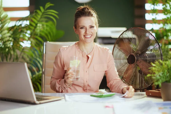持続可能な職場 幸せな現代のブックキーパー女性で現代グリーンオフィスで電気ファン 水とレモンのカップ — ストック写真