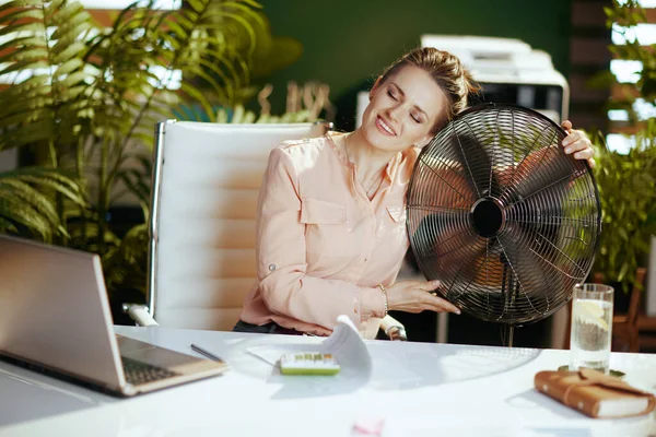 可持续工作场所 快乐的现代中年女性员工 在现代绿色办公室里 带着电扇和笔记本电脑 — 图库照片